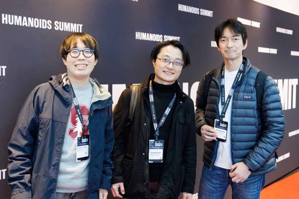 Three attendees with badges in front of the event backdrop