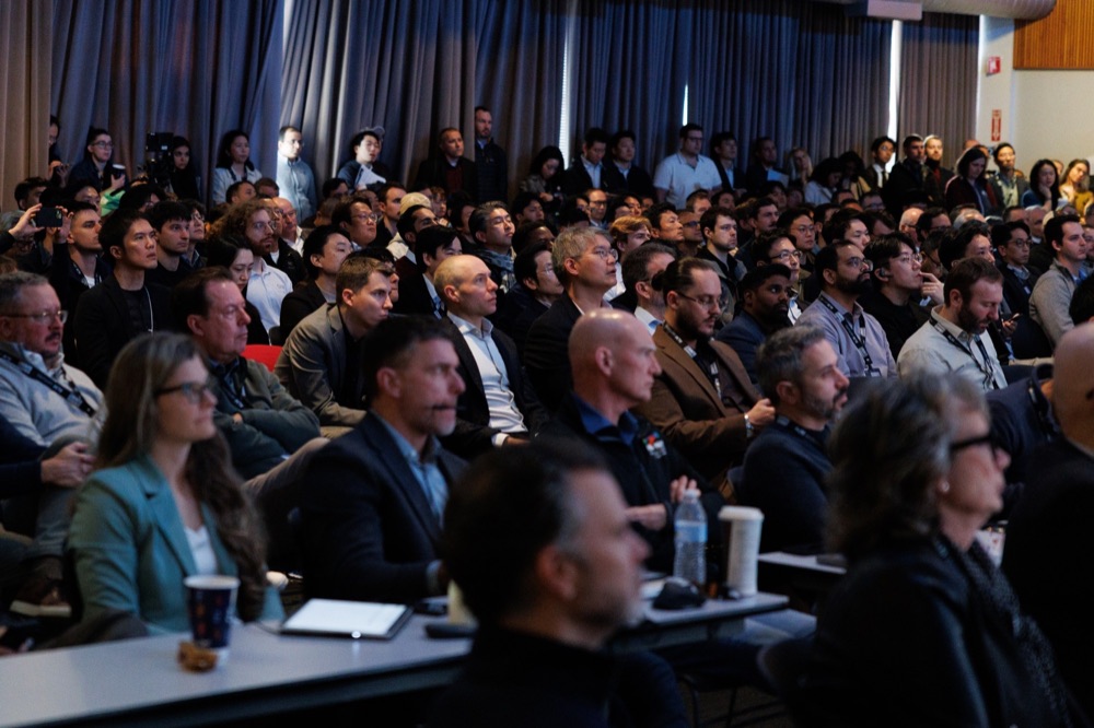 A packed audience watching a keynote, faces lit by the stage