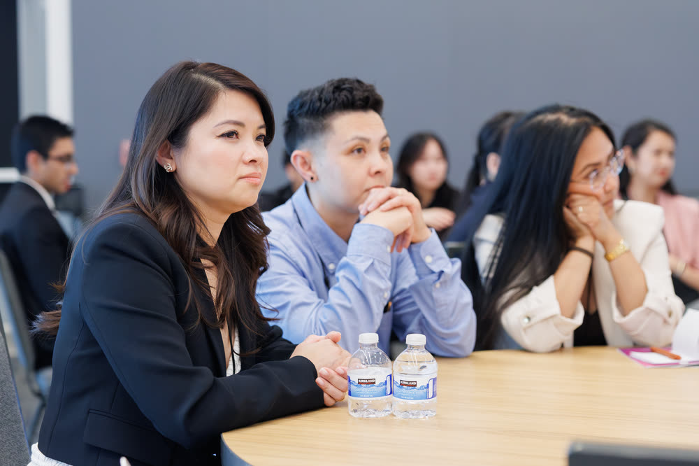 Attendees at a table listening closely, chins resting on their hands