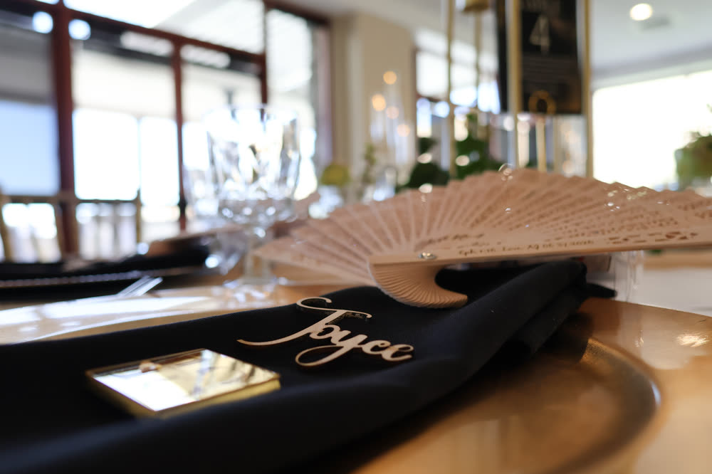 A hand-lettered name card on a black napkin beside a lace fan