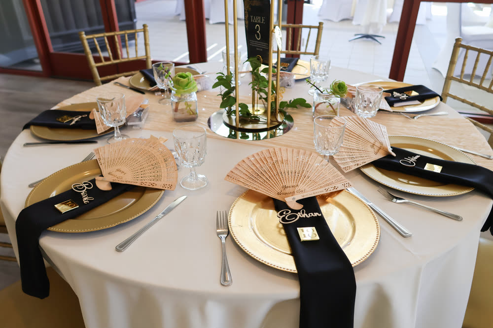 A round table set with gold chargers, black napkins and lace fans
