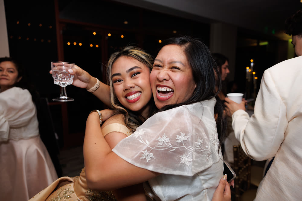 Two women hugging and laughing during a toast at an evening party