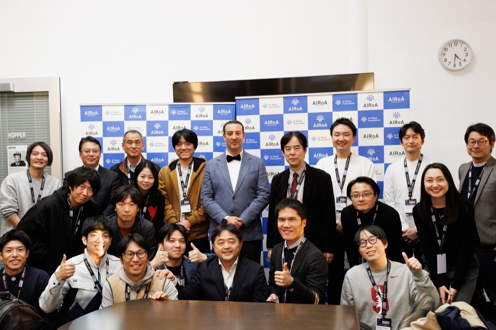 A group photo of about thirty people in front of a sponsor wall