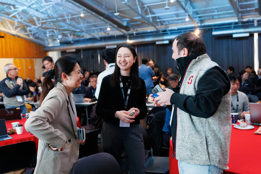 Three attendees laughing together in a busy conference hall