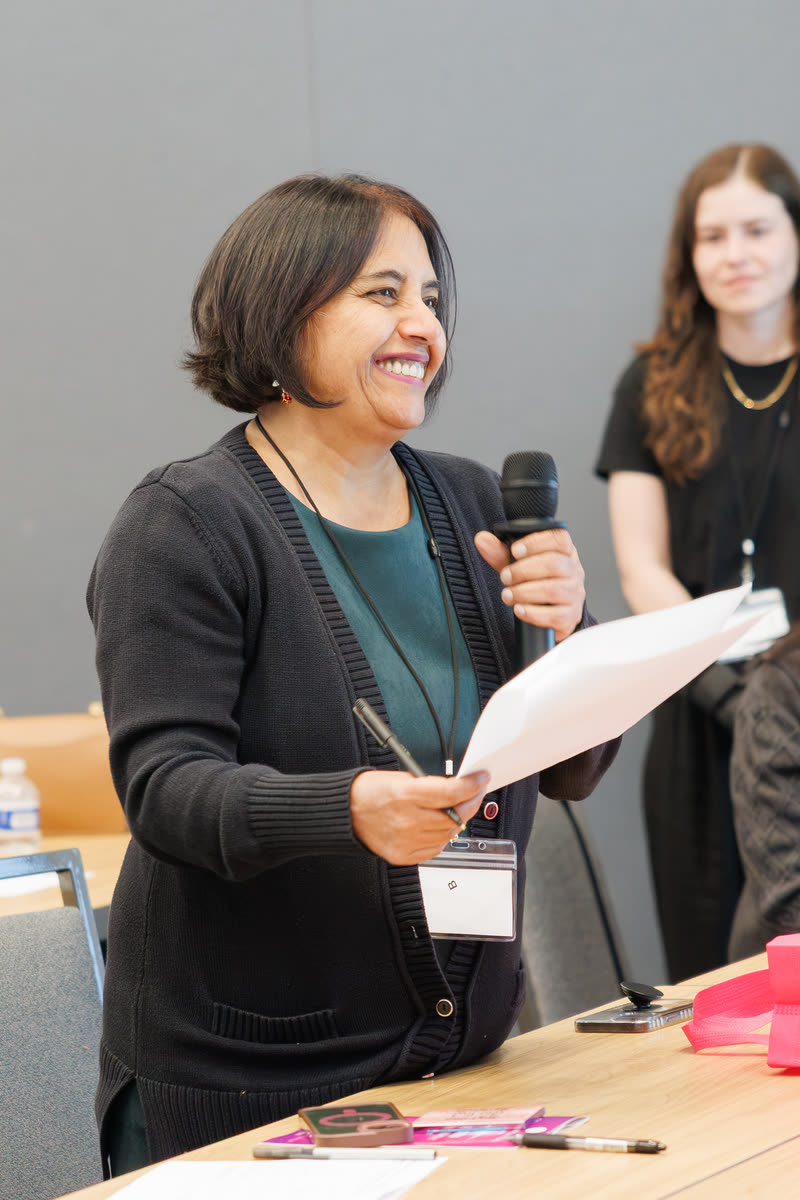 A woman laughing as she holds a mic and her notes during Q&A