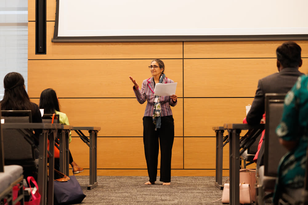 A speaker reading from her notes at the front of a wood-paneled room