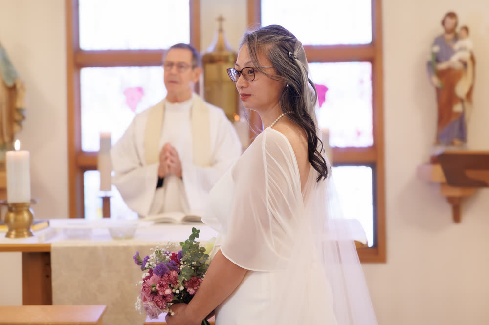 The bride at the altar, holding a bouquet, with the priest behind her