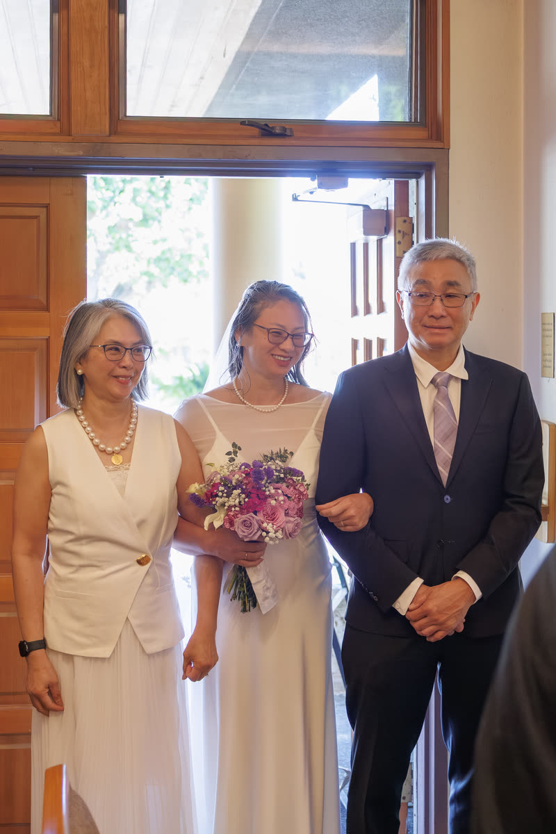 A bride in white walking down the aisle between her parents