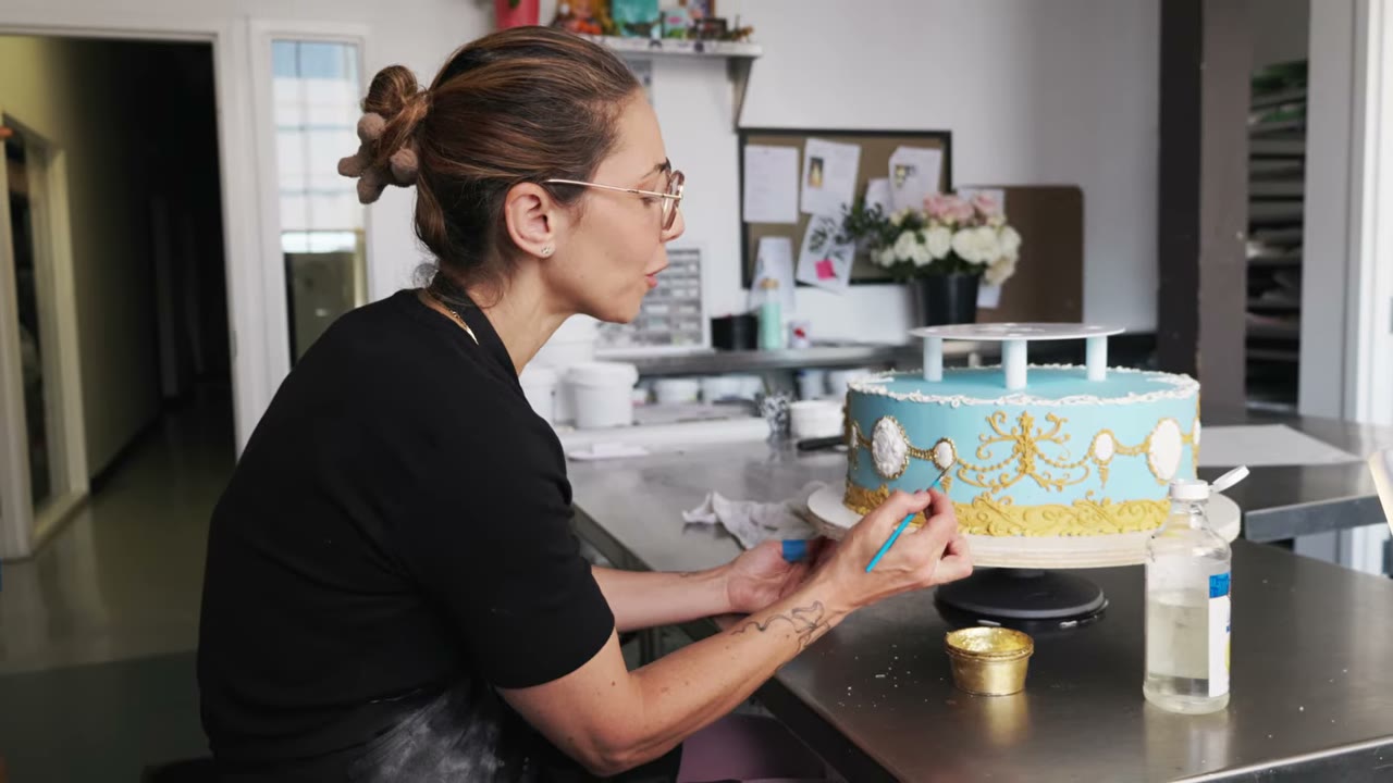 The owner of Cake Coquette decorating a blue and gold cake in her San Francisco studio