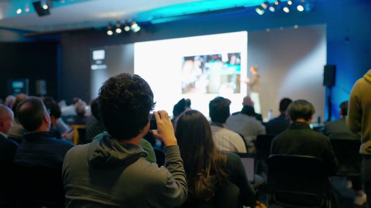 Attendees filming a presentation on stage at a conference